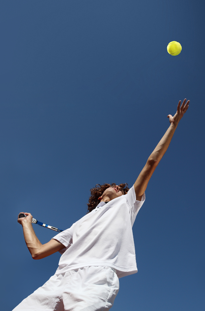 Tennis player serving a ball overhead.